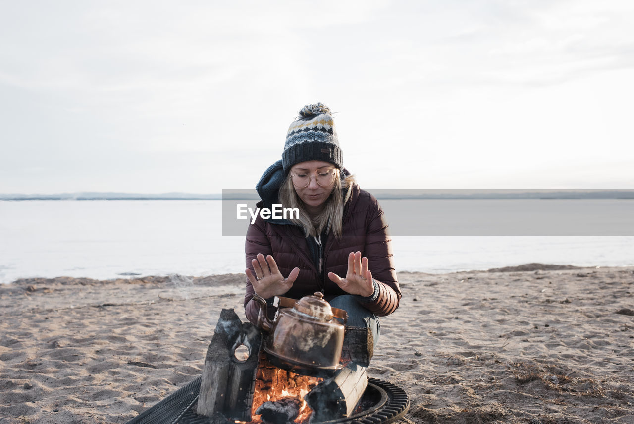 Woman warming her hands on a camp fire waiting for water to boil