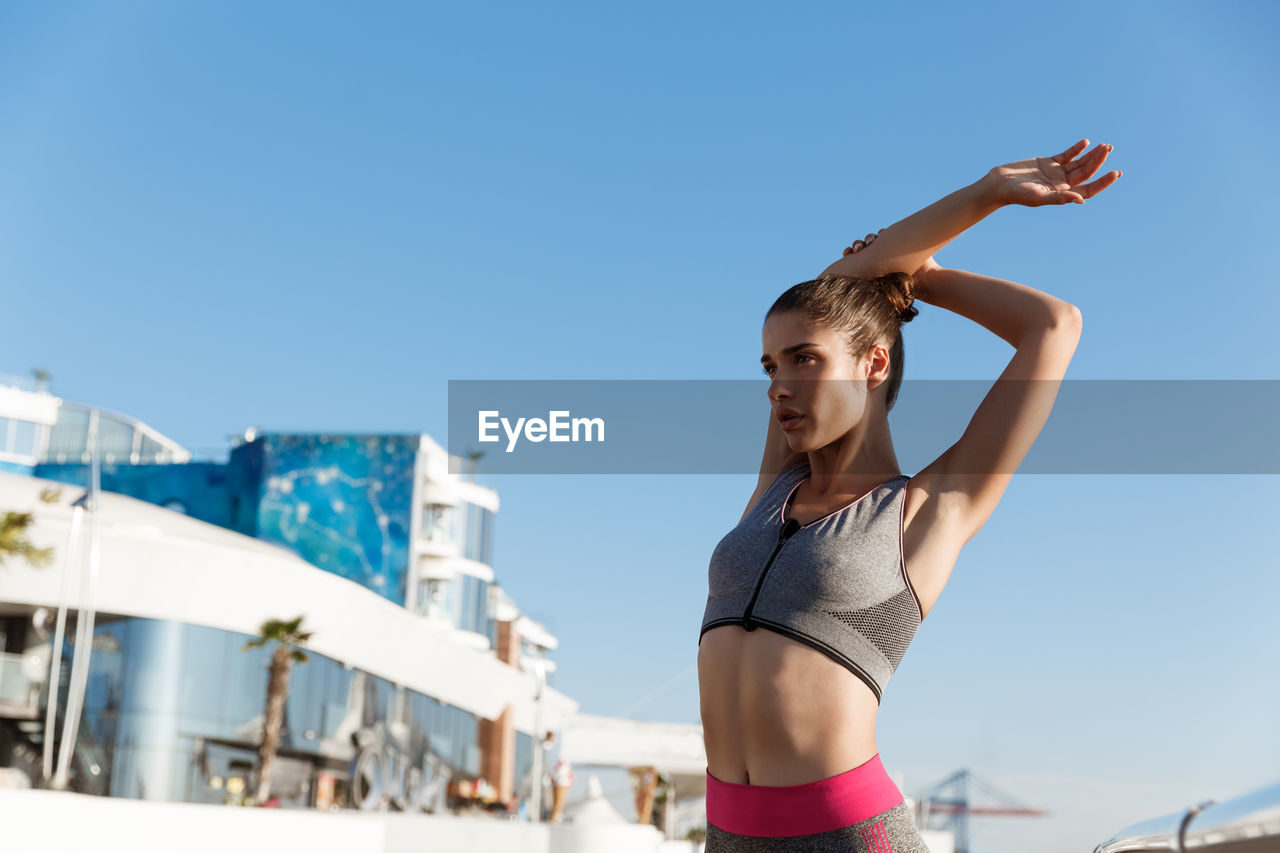 Woman exercising while standing against sea and sky