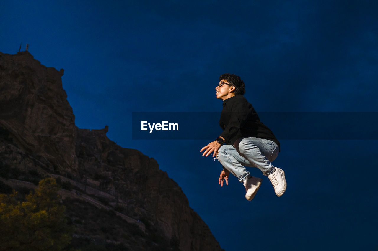 Young transgender man jumping outdoors at night.