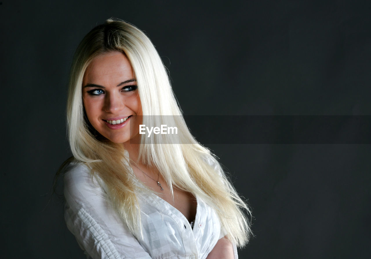 Beautiful smiling woman looking away while sitting against black background