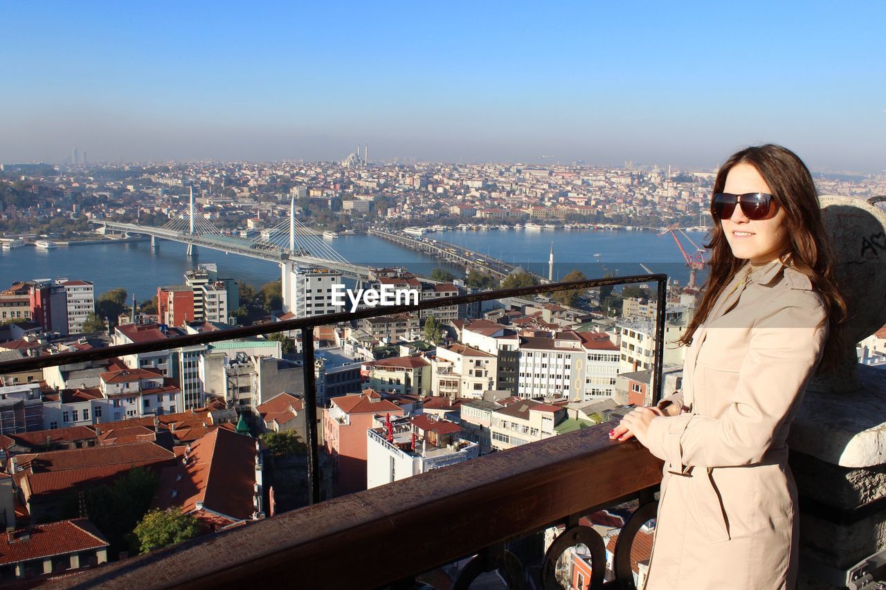 Smiling woman looking at city with golden horn metro bridge in background against clear blue sky