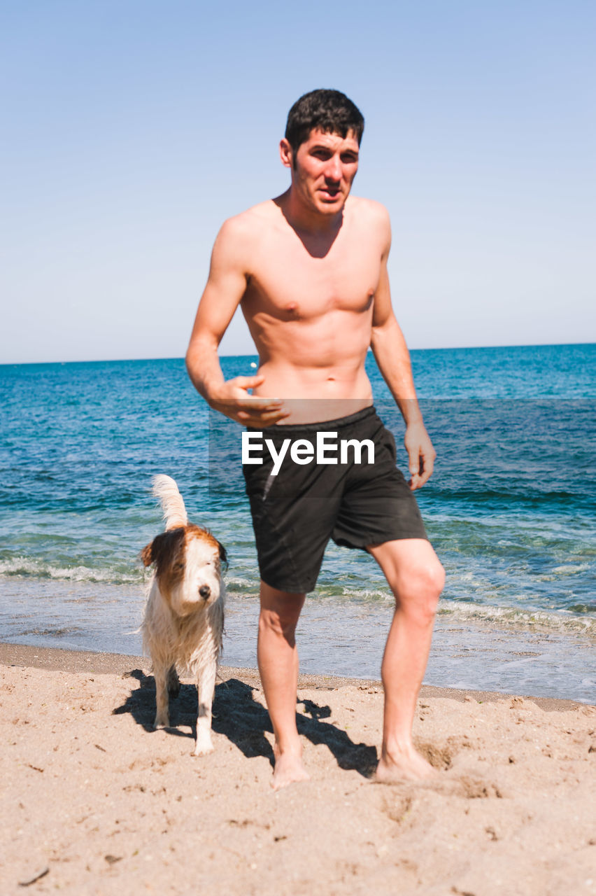 Shirtless man walking with dog at beach