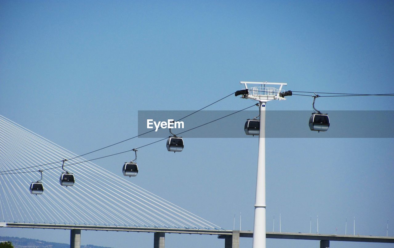 Low angle view of overhead cable cars against clear blue sky