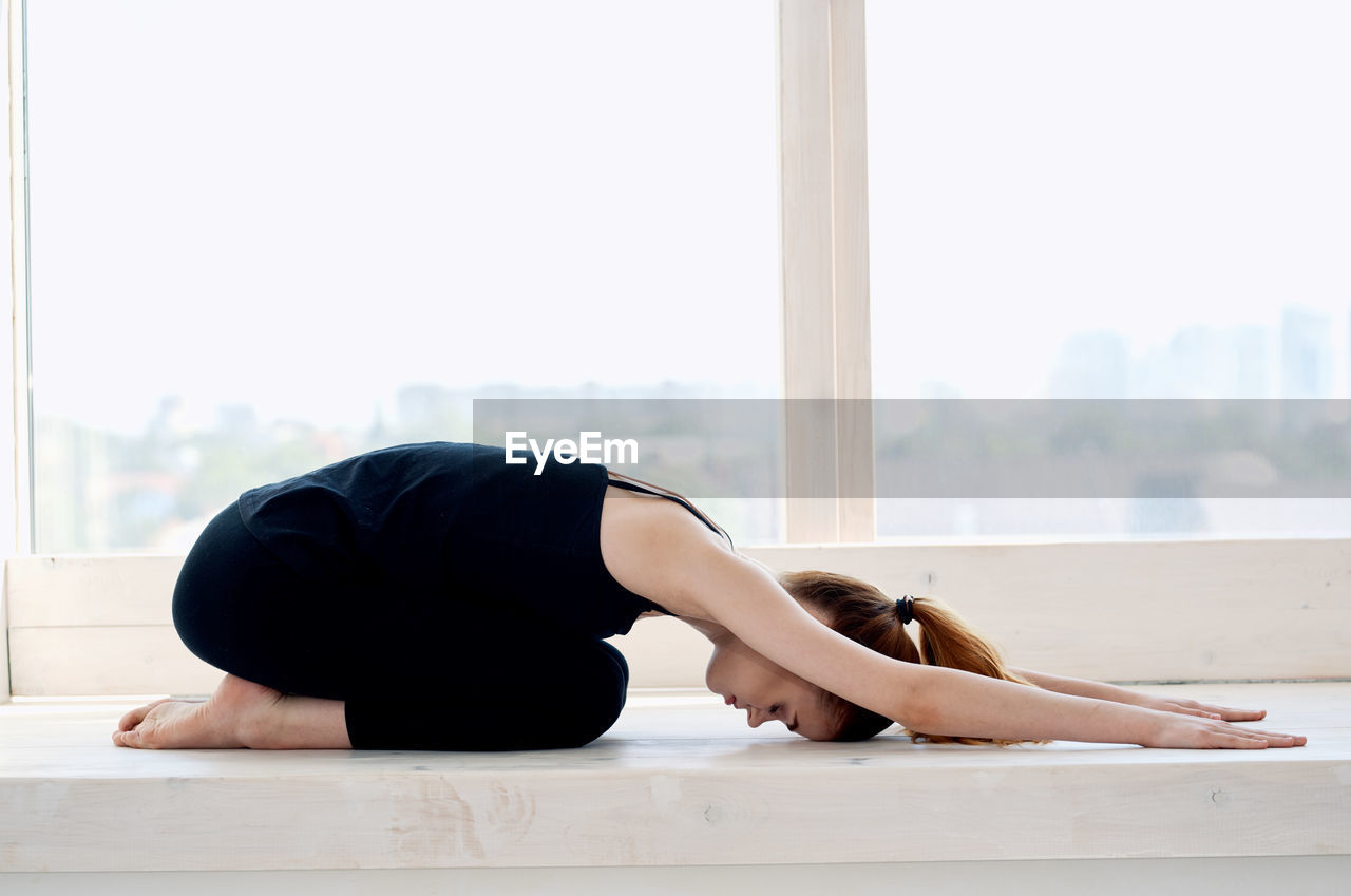 Full length of young woman relaxing on floor against window