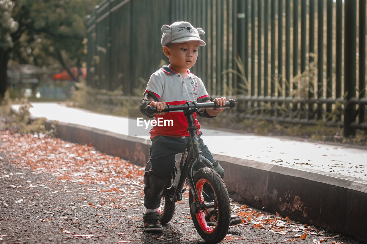 childhood, child, one person, full length, men, transportation, bicycle, sports, helmet, vehicle, nature, day, leisure activity, lifestyles, spring, headwear, casual clothing, clothing, cycling, toddler, outdoors, activity, person, sports helmet, smiling, innocence, cute, architecture, front view, emotion, cycle sport, land vehicle, happiness, motion, standing, wheel