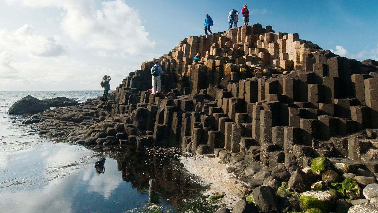 Low angle view of people standing on giants causeway against sea