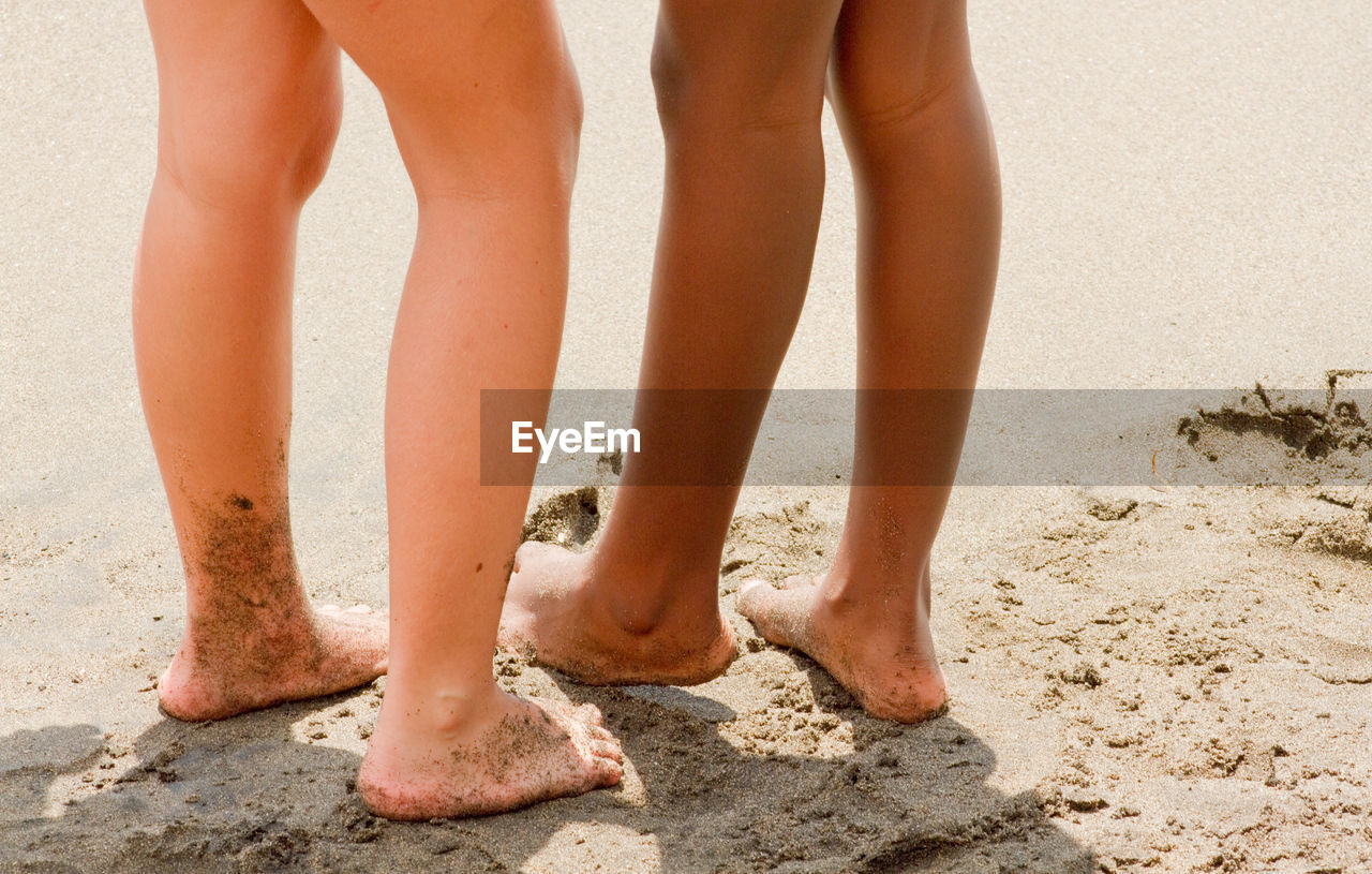 Low section of friends standing on sandy beach