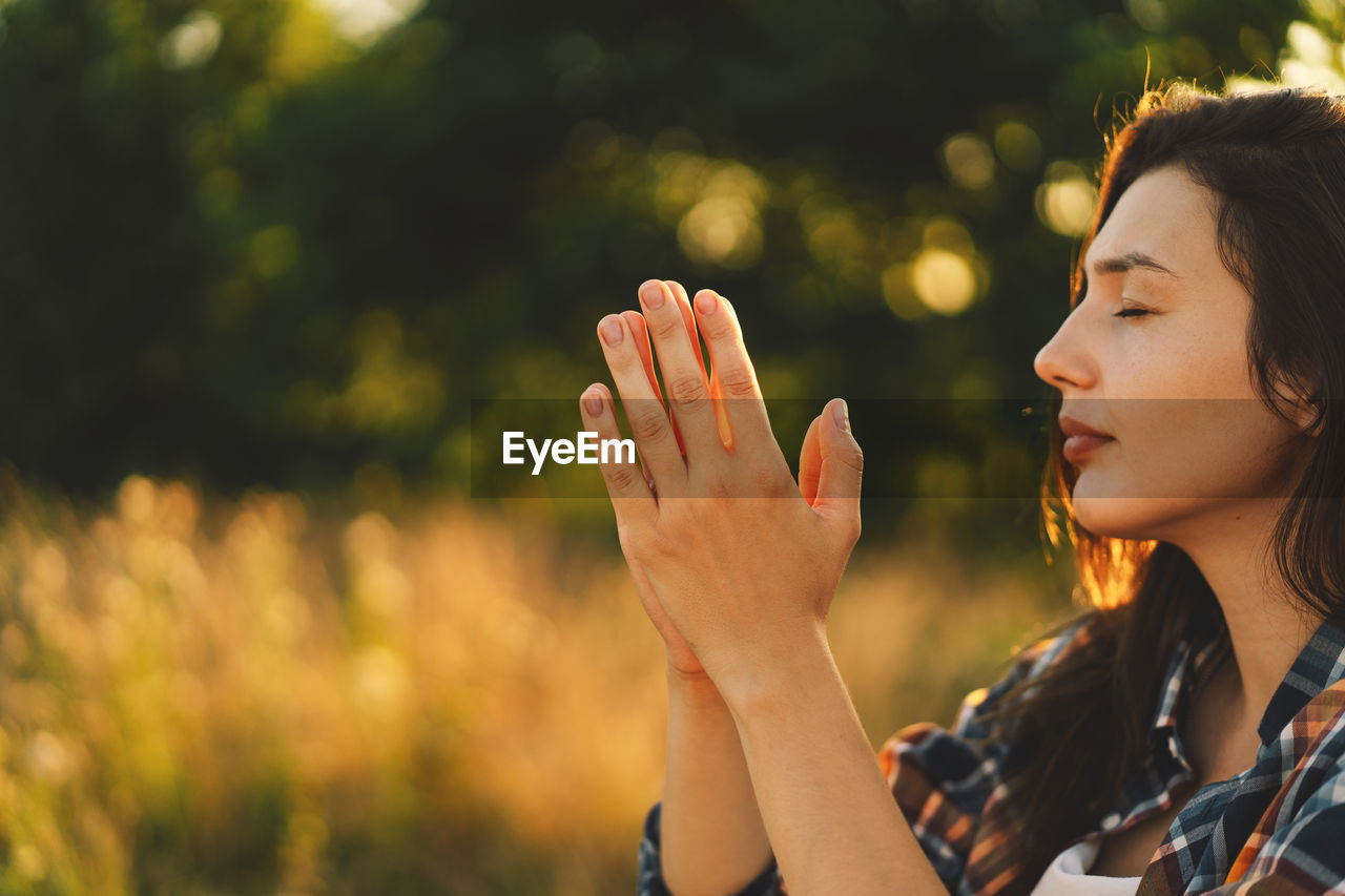 Woman closed her eyes, praying in a field during beautiful sunset.