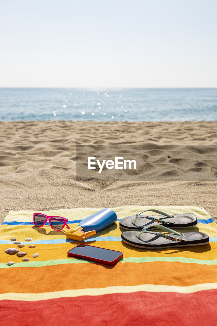 Towel, sunscreen, flip-flops, sunglasses and smart phone on the beach. summer concept.