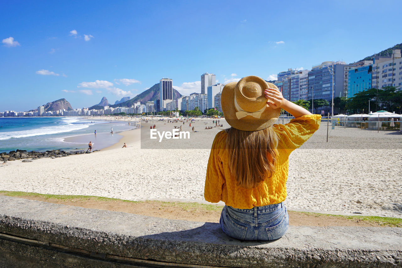 Beautiful young woman sitting on wall enjoying the cityscape of rio de janeiro, brazil