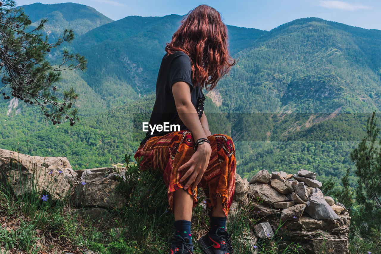 REAR VIEW OF WOMAN STANDING ON MOUNTAIN