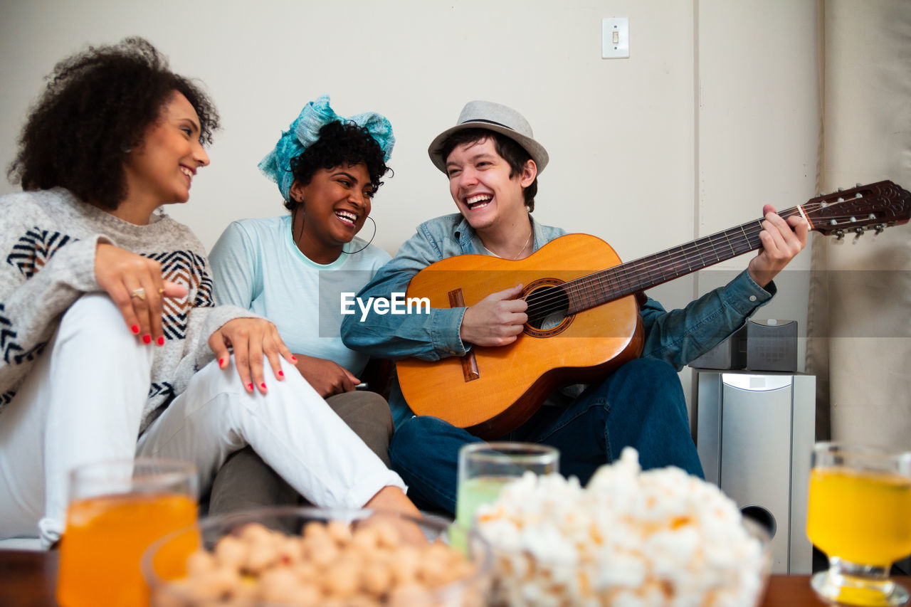 Man playing guitar while sitting with female friends at home