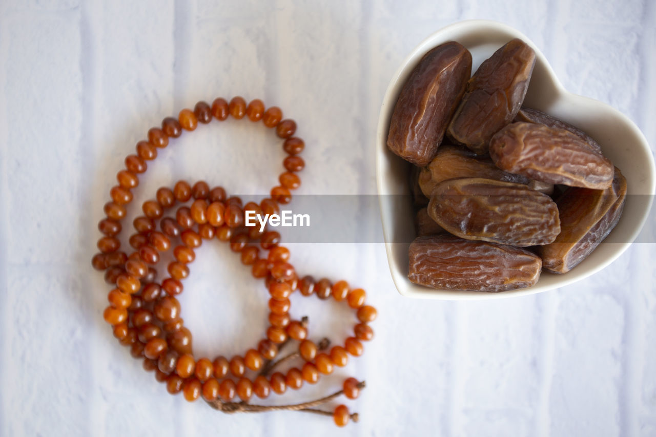 High angle view of dates in heart shape bowl by prayer beads on table