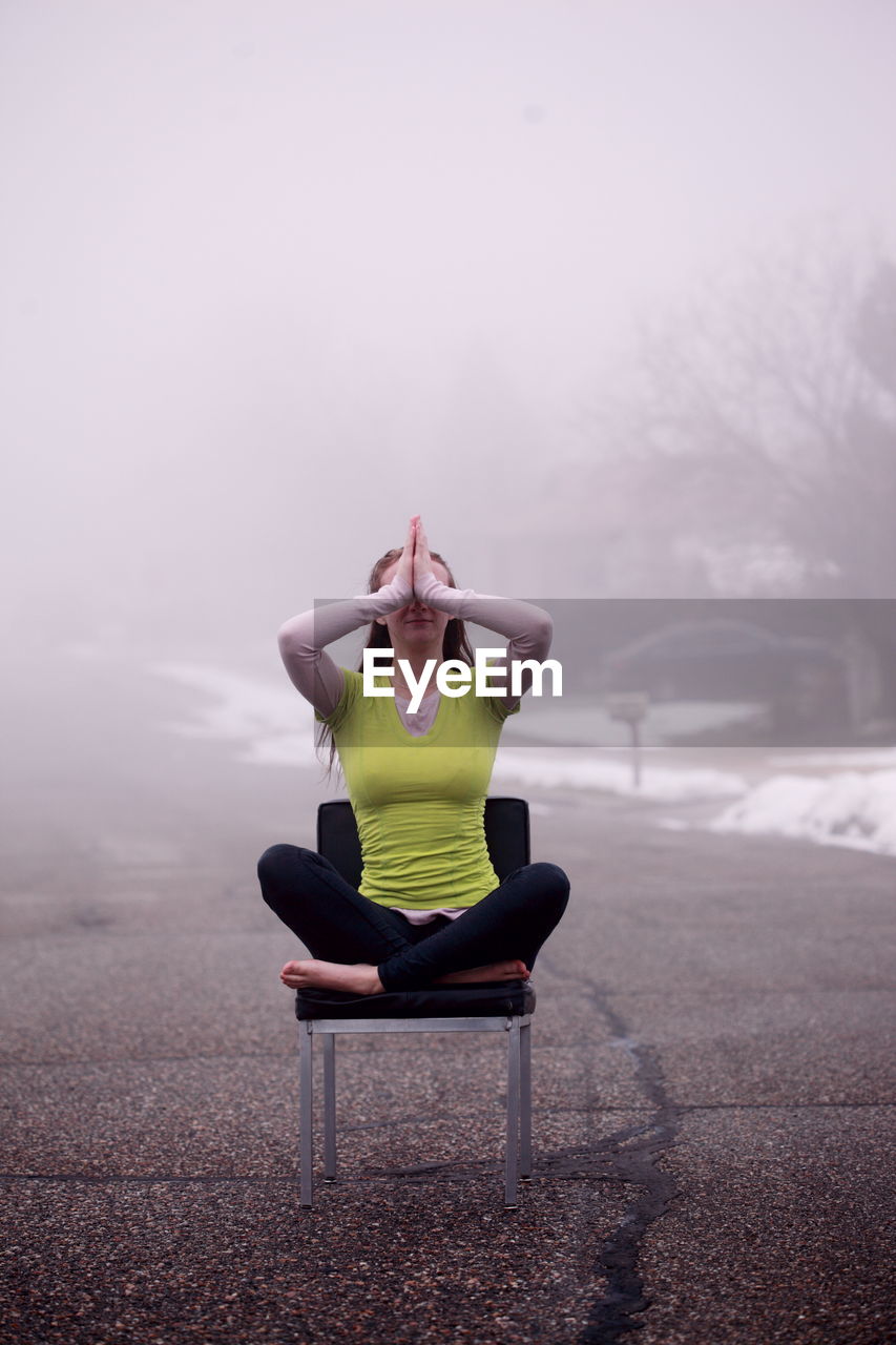 Beautiful young woman doing yoga on chair during foggy weather