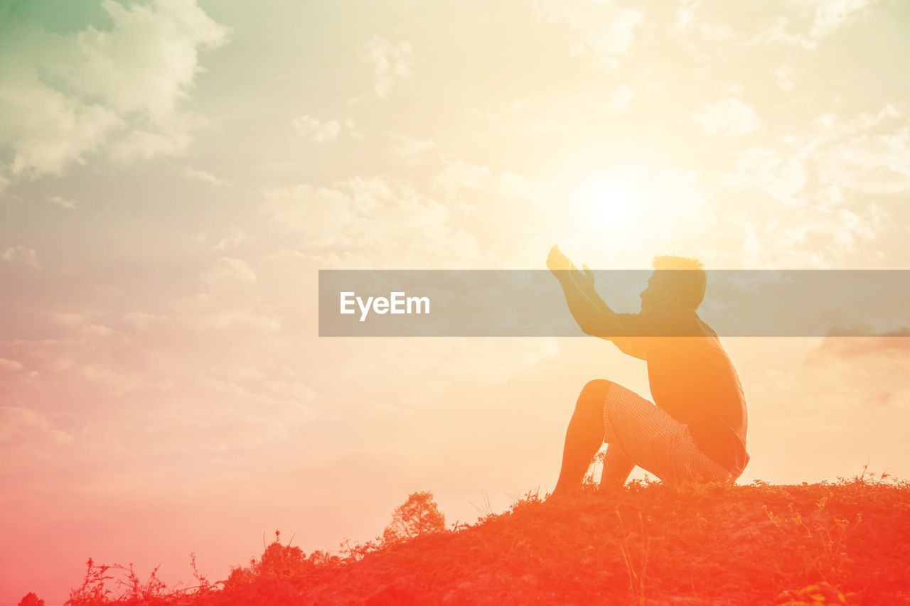 SIDE VIEW OF SILHOUETTE MAN SITTING AGAINST ORANGE SKY