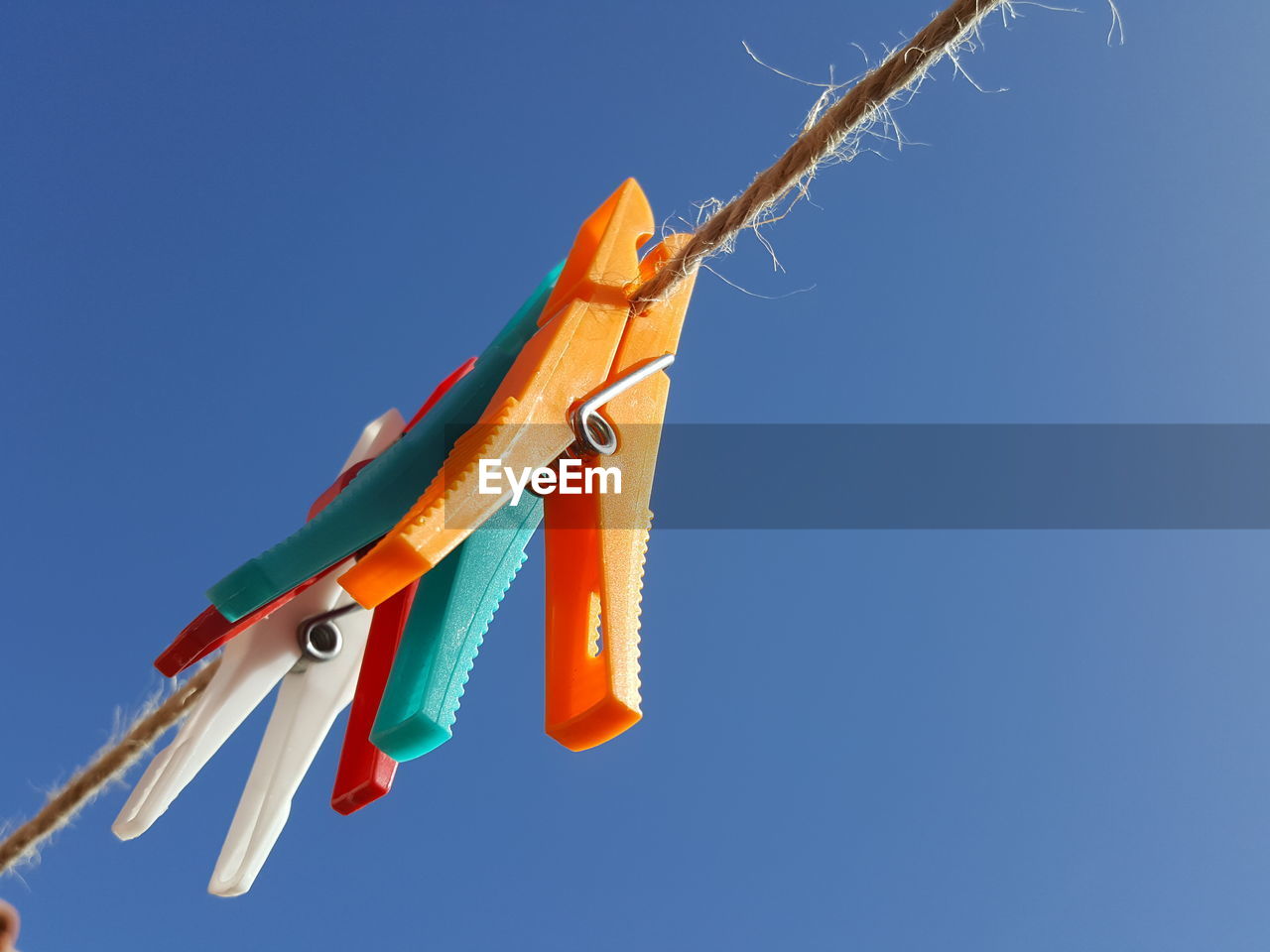 Low angle view of clothespins hanging against clear blue sky