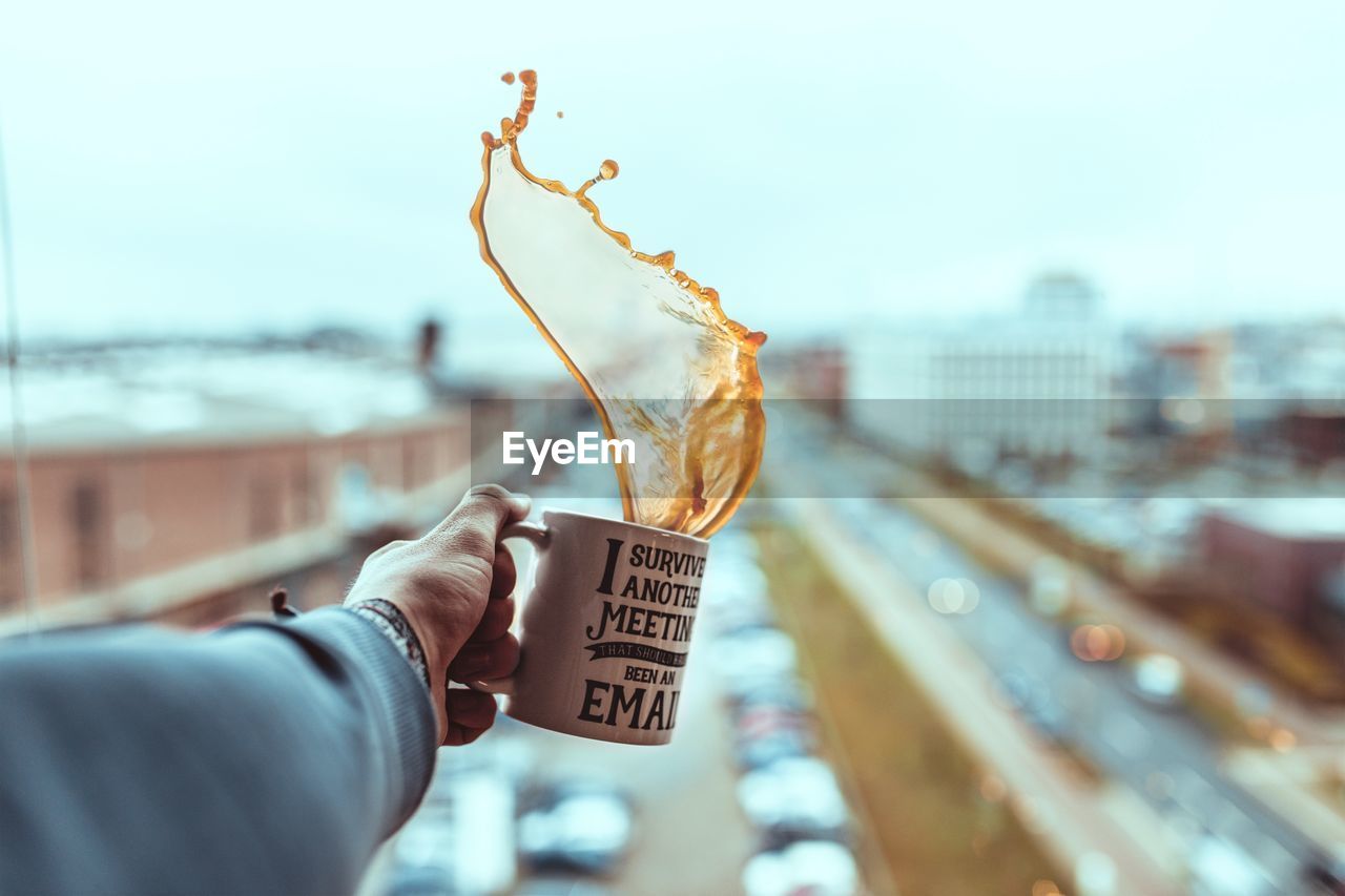 Cropped hand holding coffee cup against sky