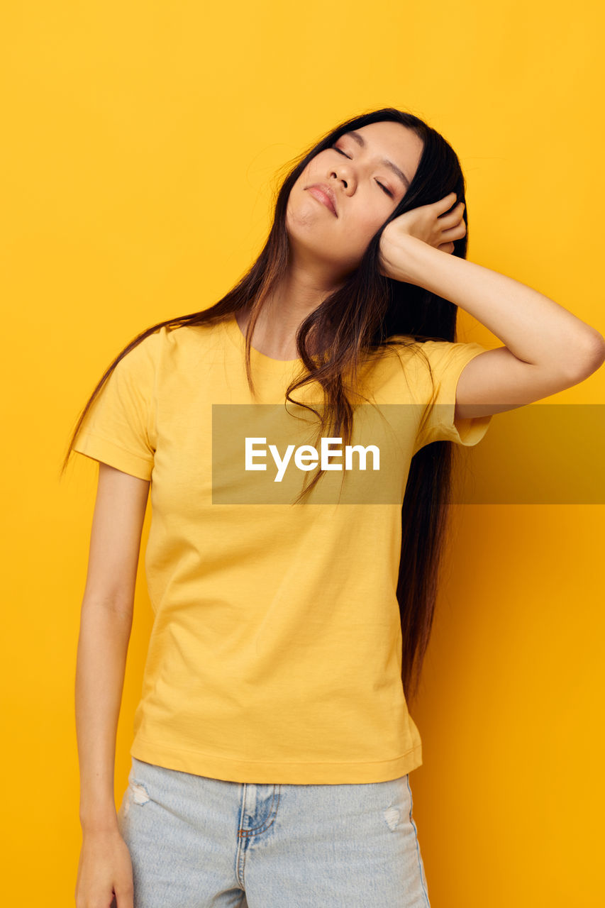 Portrait of young woman standing against yellow background