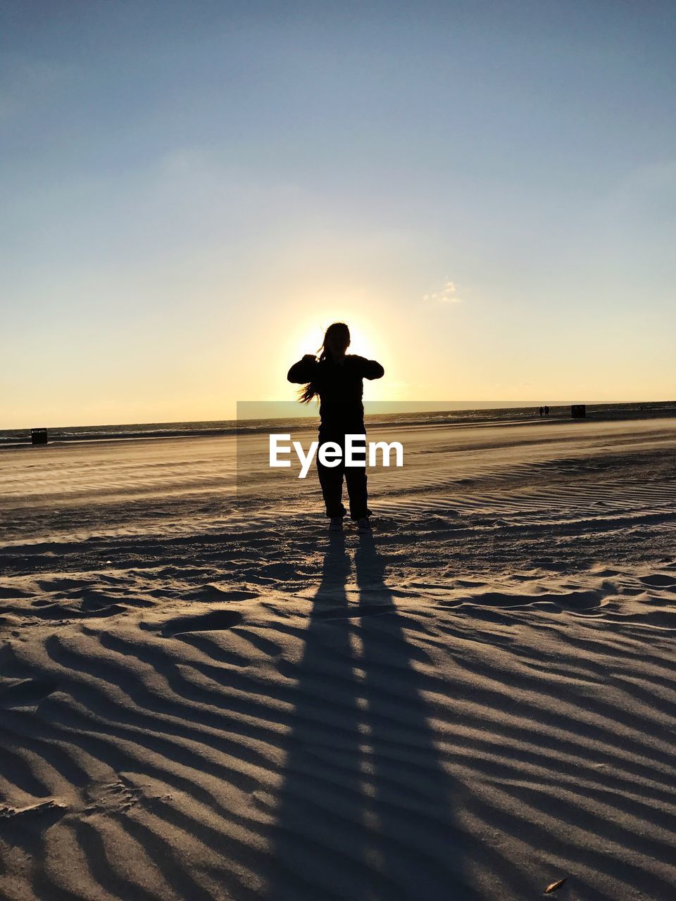 Silhouette woman standing on sea shore at beach against clear sky during sunset