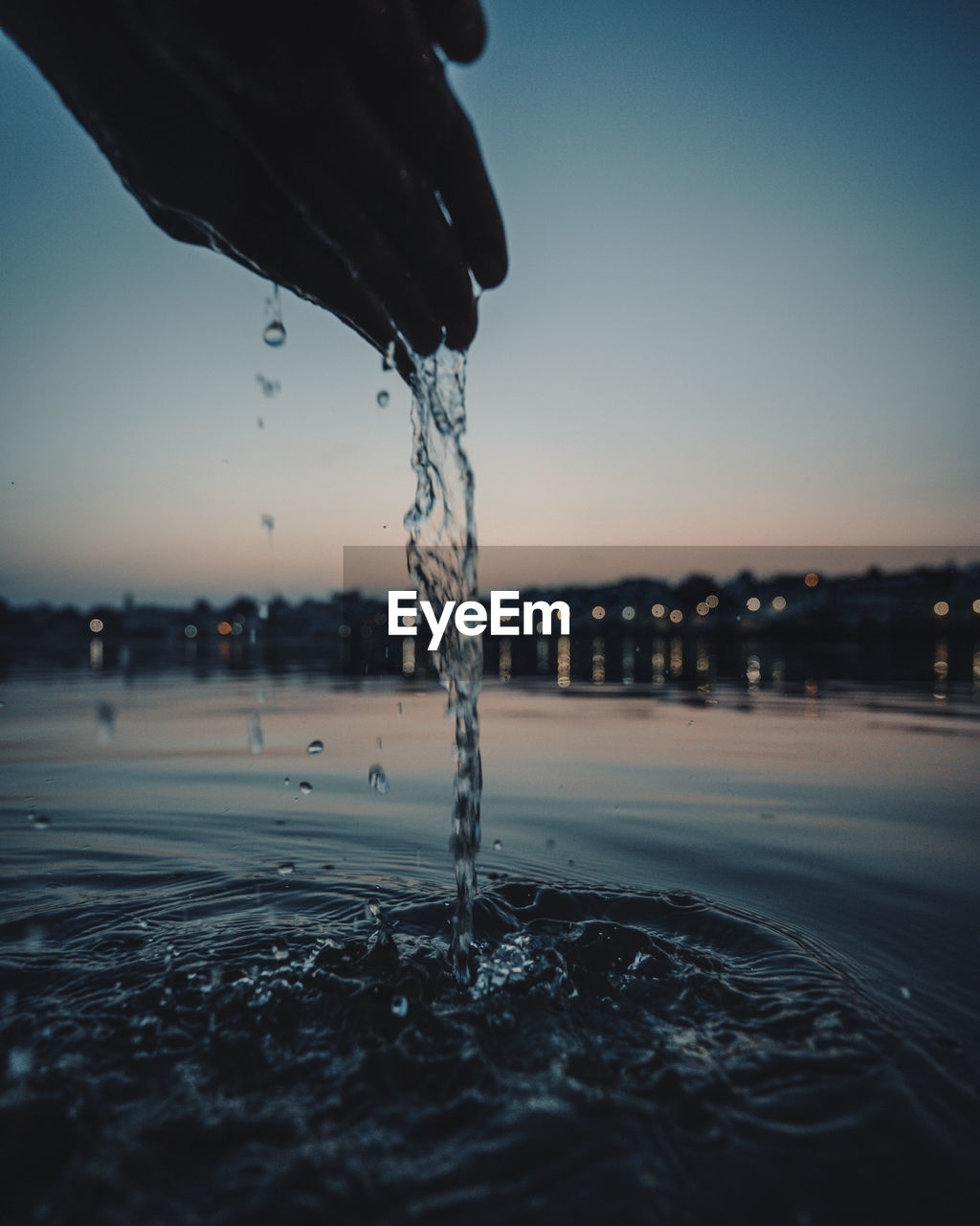 Close-up of hand splashing water against clear sky