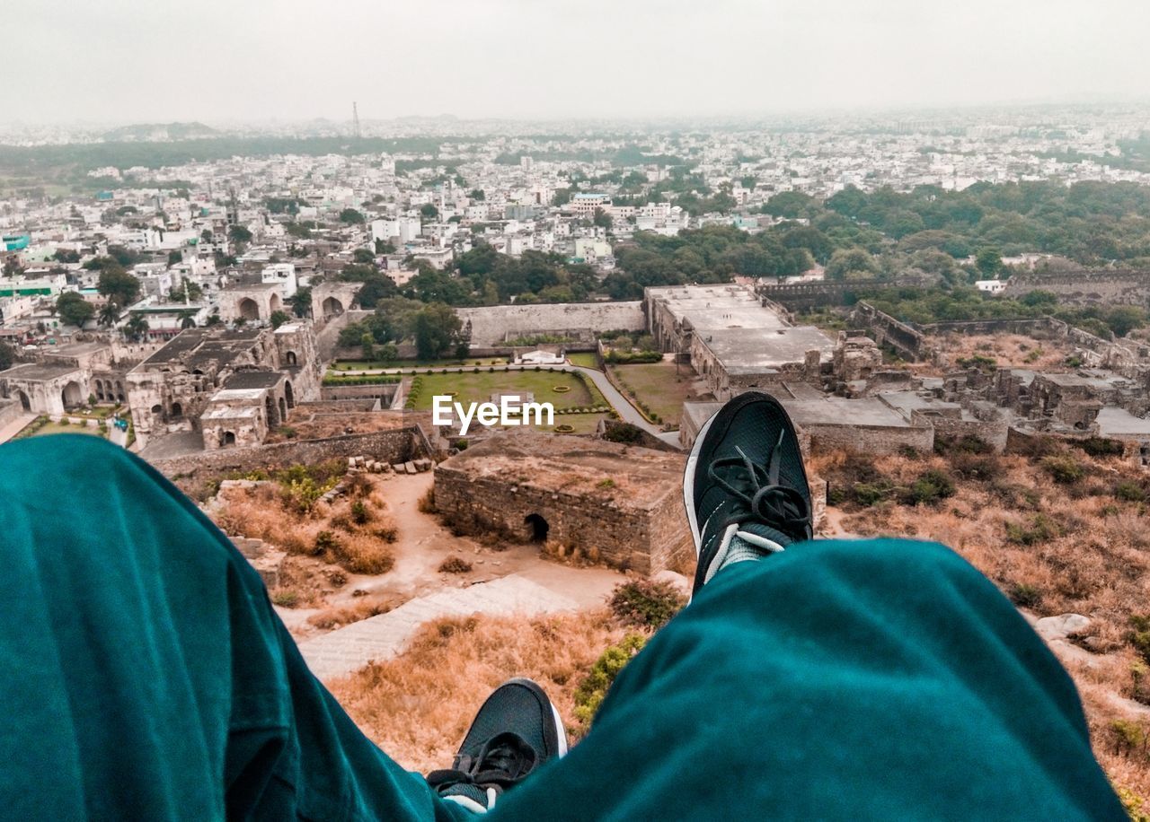 Low section of man sitting on mountain against cityscape