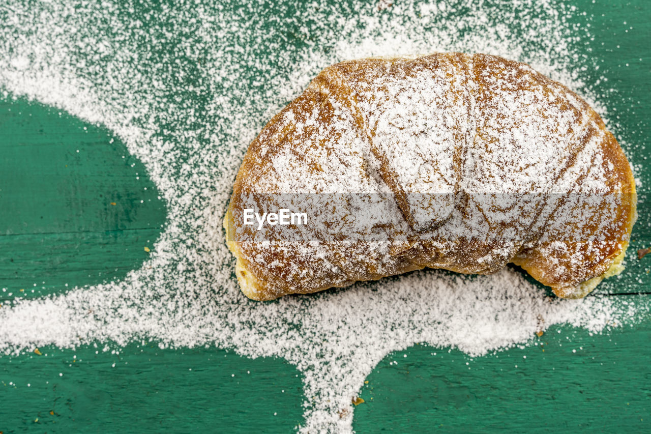 Freshly baked croissants with powdered sugar on a green rustic table ready for breakfast. top view