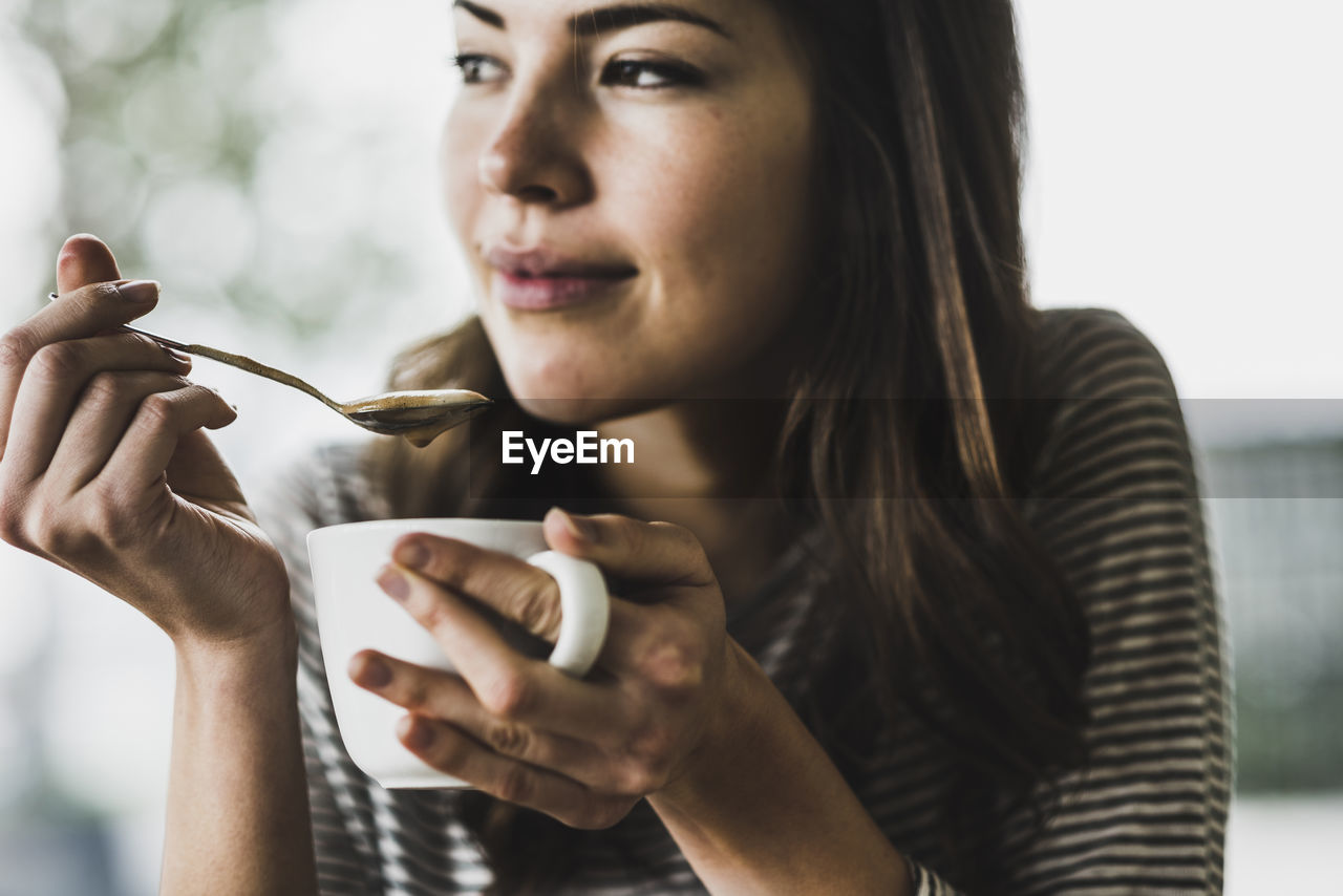 Young woman drinking cappuccino, spooning milk froth
