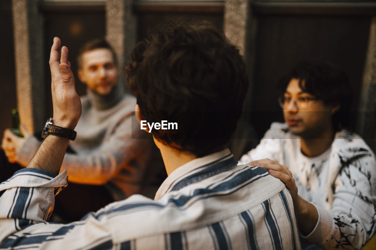 Rear view of man gesturing while talking with friends at balcony