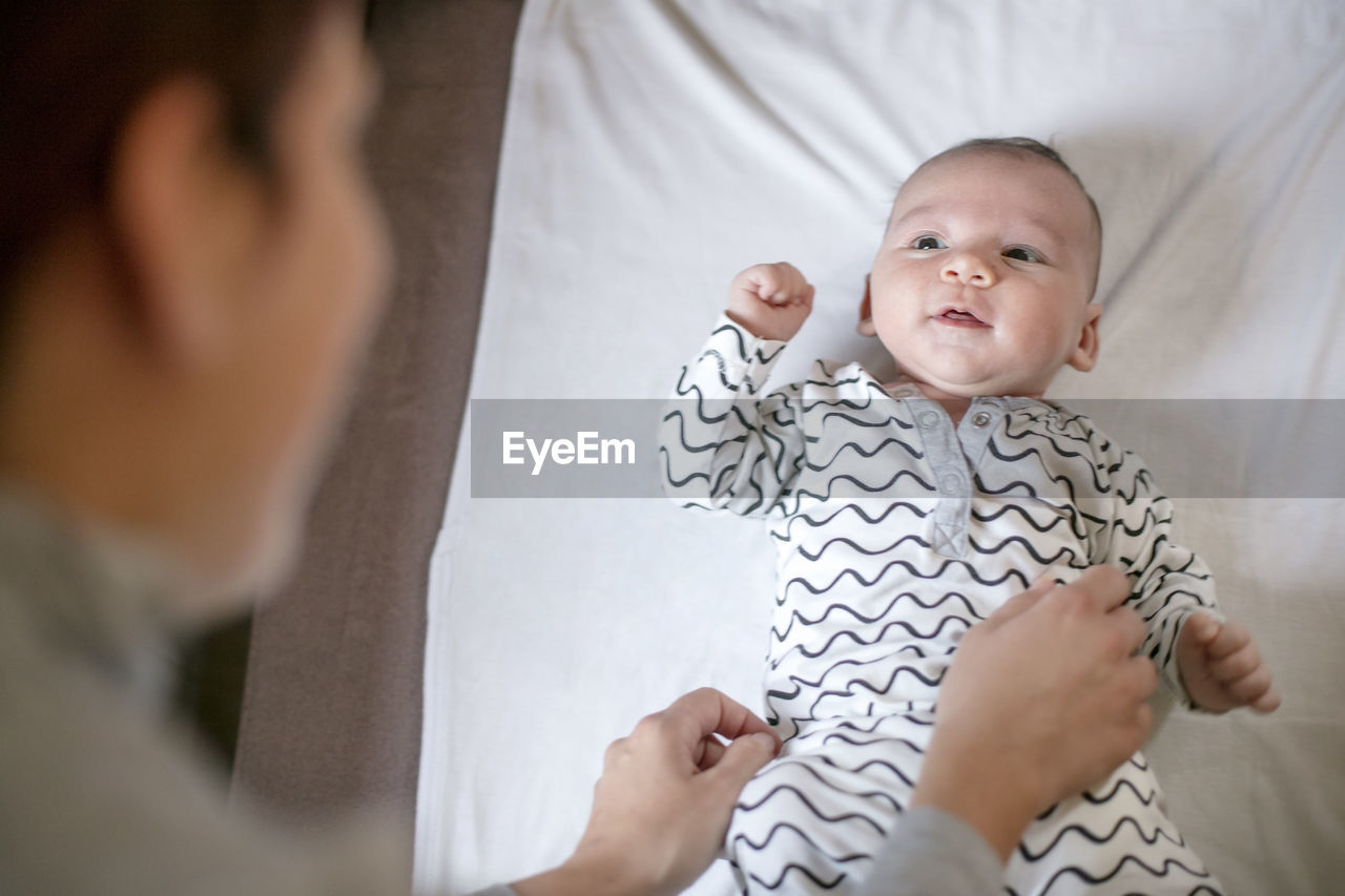 High angle view of mother adjusting baby boy clothing at home