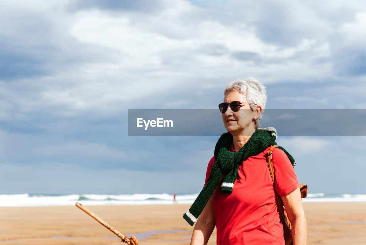 Senior female trekker walking on sandy shore against endless sea during trip