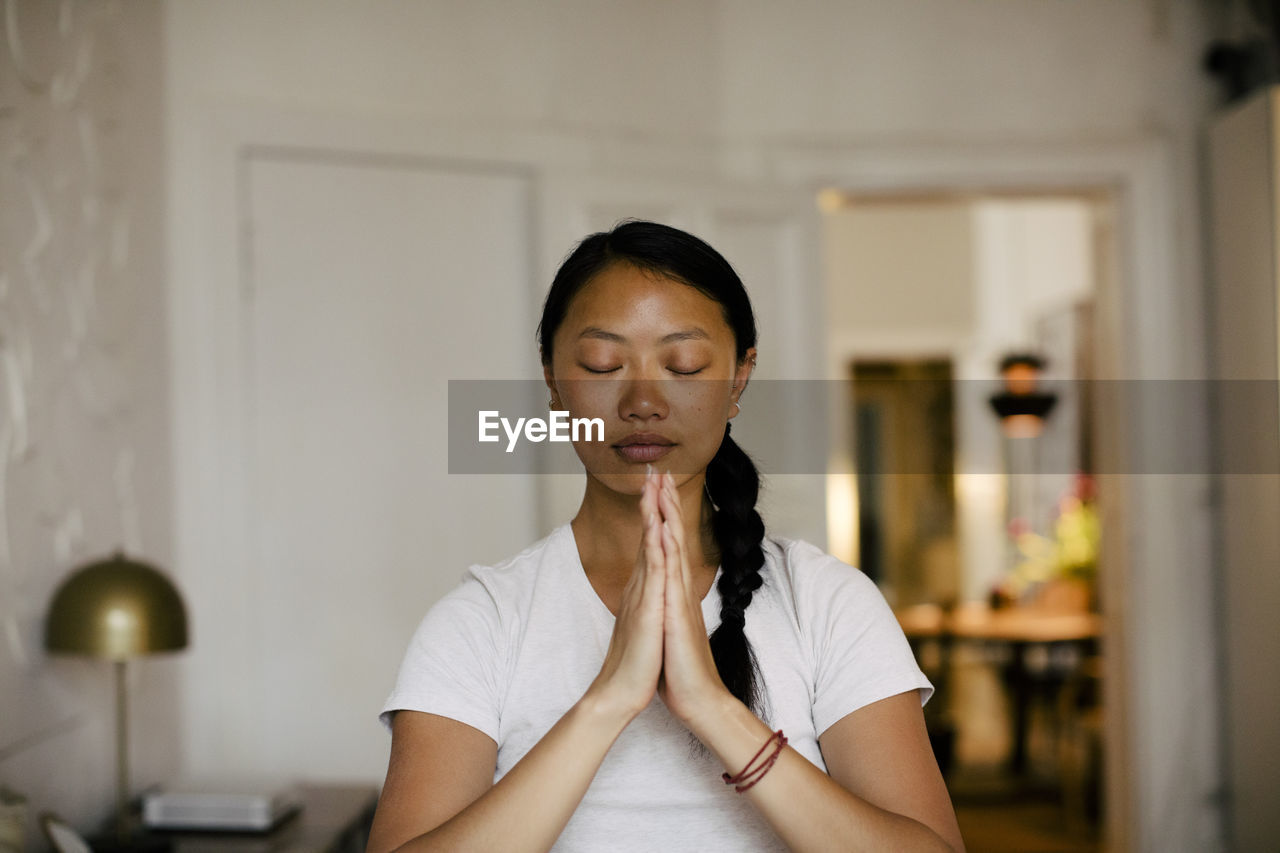 Young woman with hands clasped meditating at home