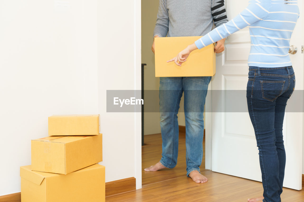 Low section of man holding box by woman pointing while standing on hardwood floor
