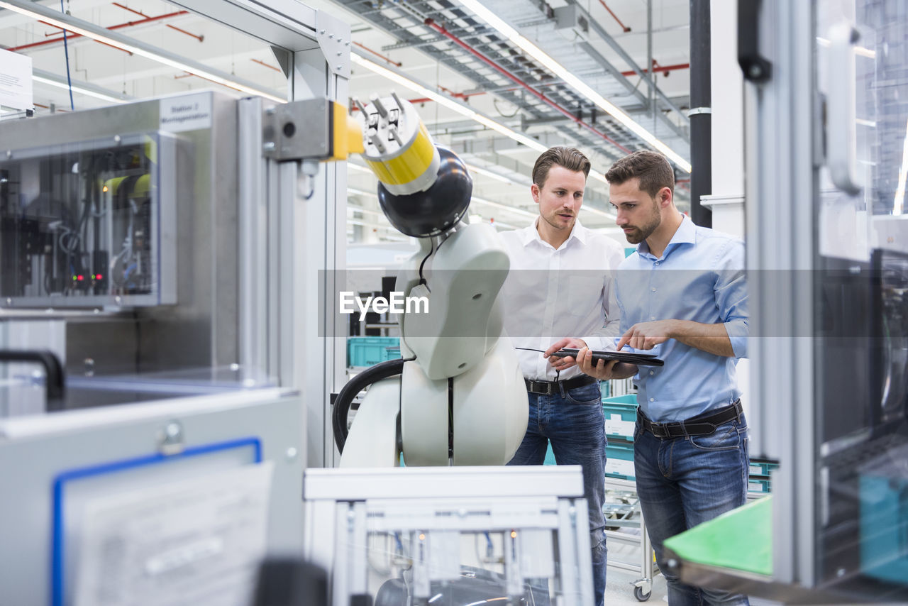 Two men with tablet examining assembly robot in factory shop floor