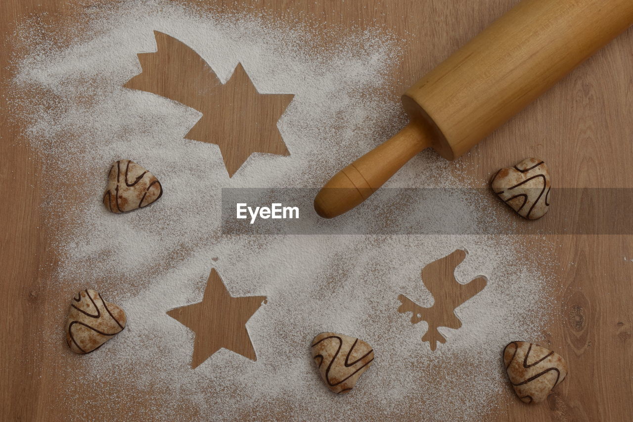 High angle view of cookies, flour and rolling pin on wooden background