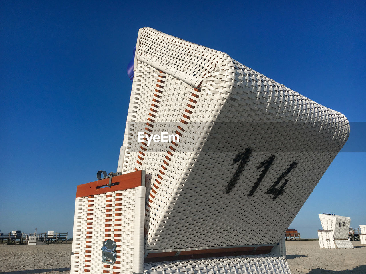 Traditional north german white beach chair with black number 114 at north sea beach against blue sky