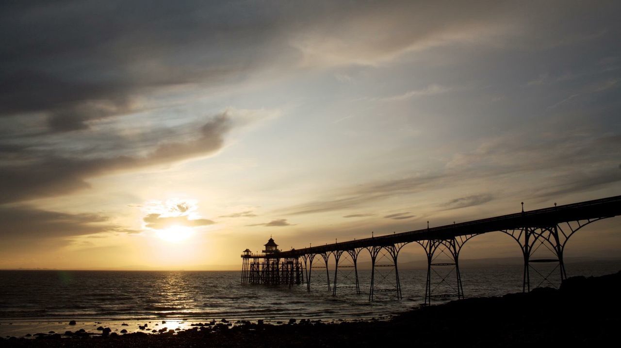 Silhouette clevedon pier over sea against sky at sunset