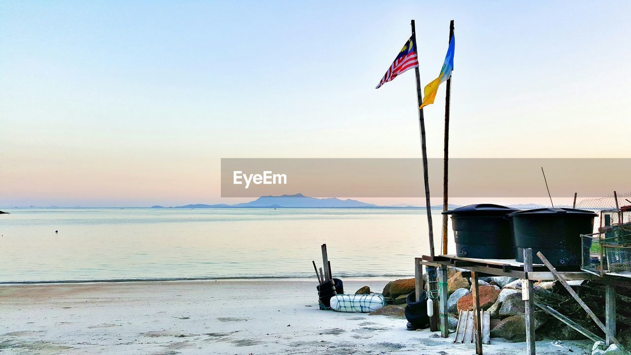 Flags at beach against sky during sunset