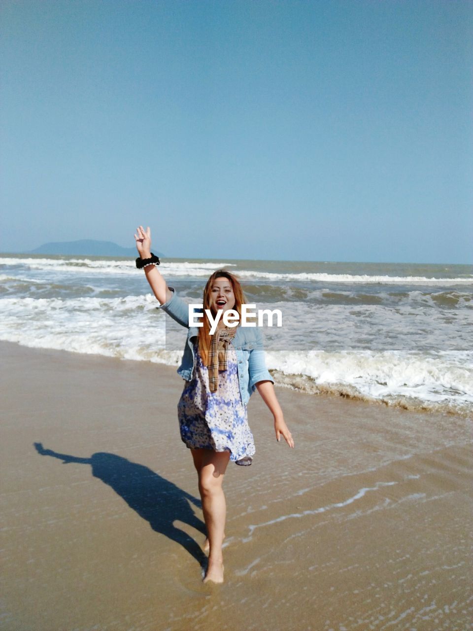 Happy young woman walking at beach against clear sky