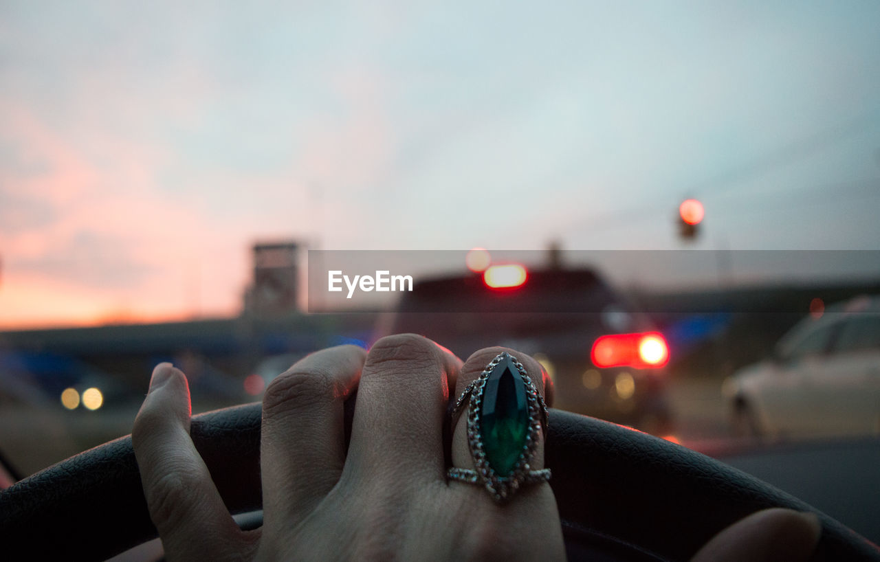 Cropped hand of woman driving car during sunset