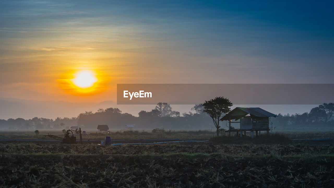 Farm against sky during sunset