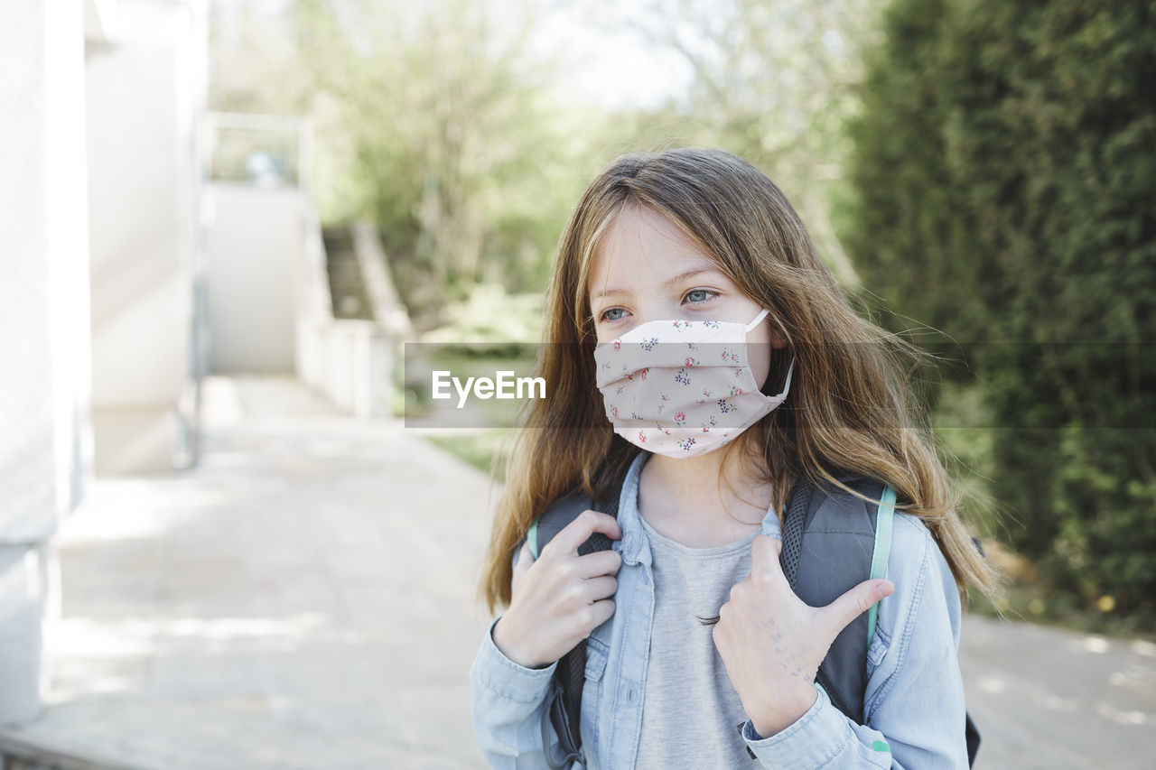 Girl wearing mask while standing with backpack