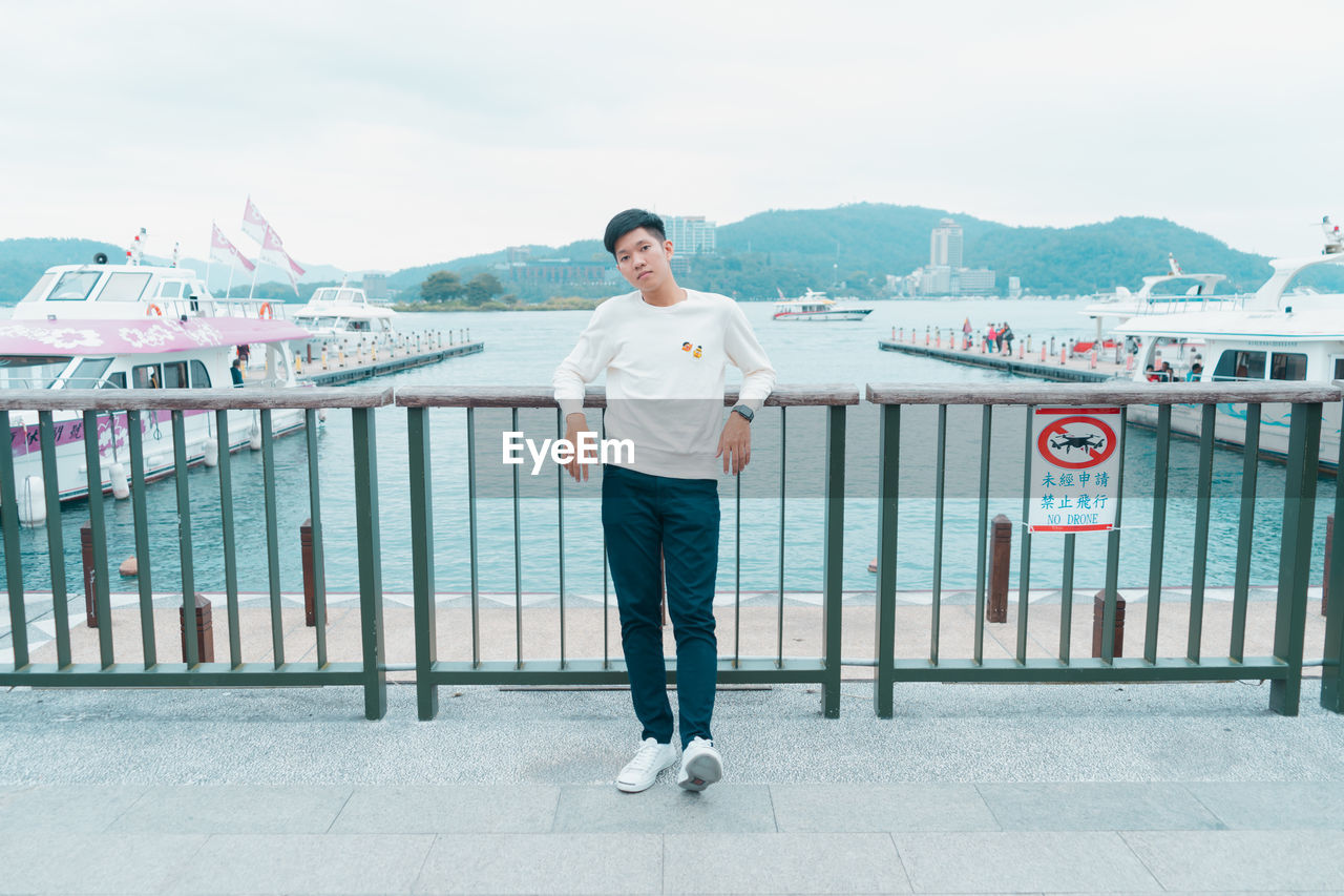 PORTRAIT OF YOUNG MAN STANDING AGAINST RAILING