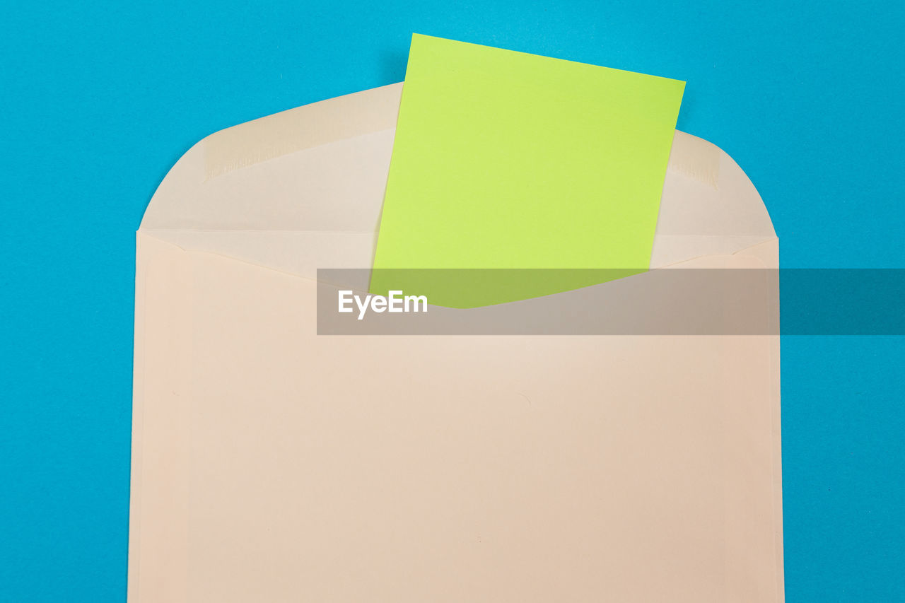CLOSE-UP OF YELLOW PAPER AGAINST BLUE BACKGROUND AGAINST WHITE WALL