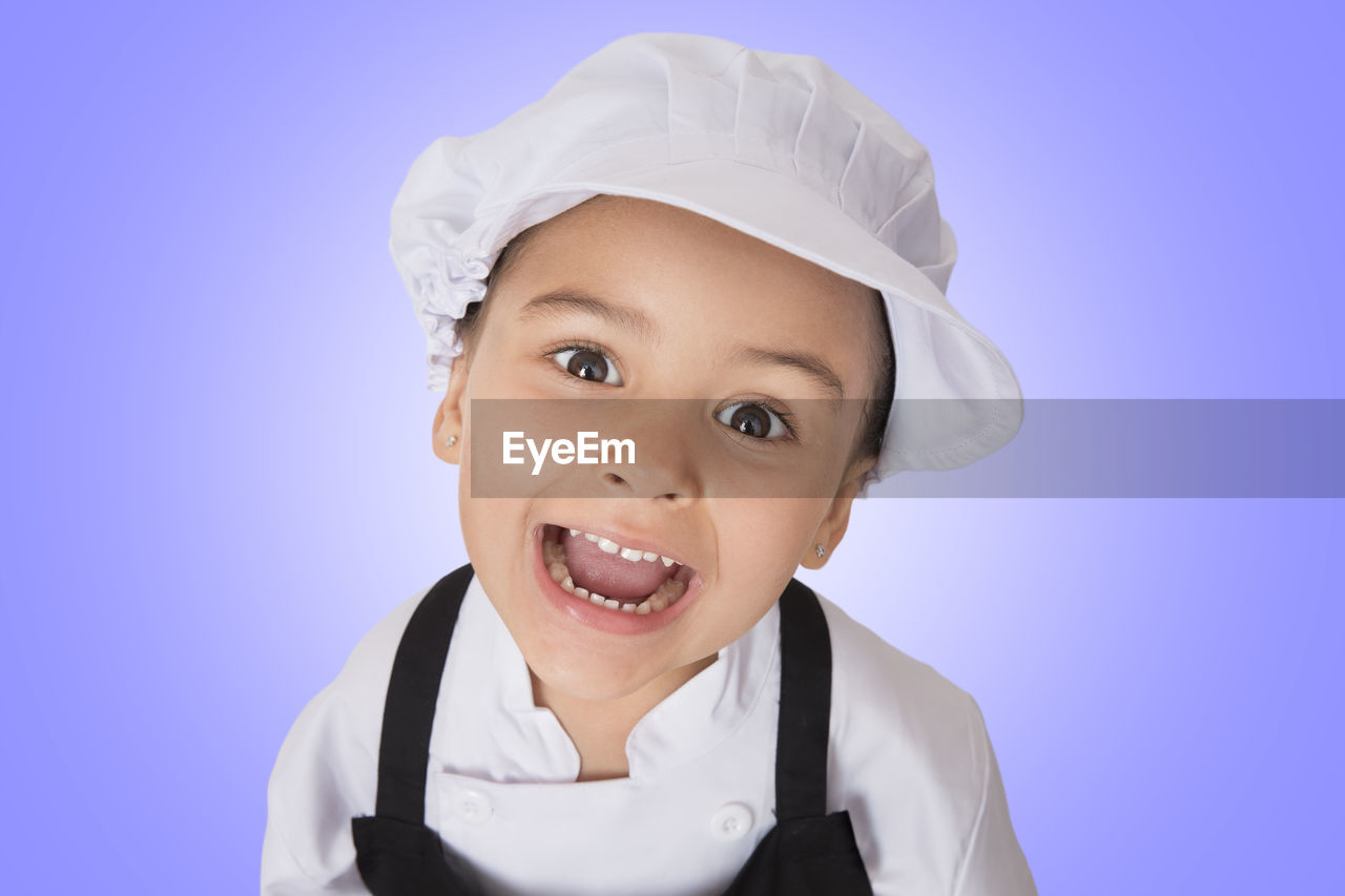 Portrait of girl in chef uniform standing against purple background