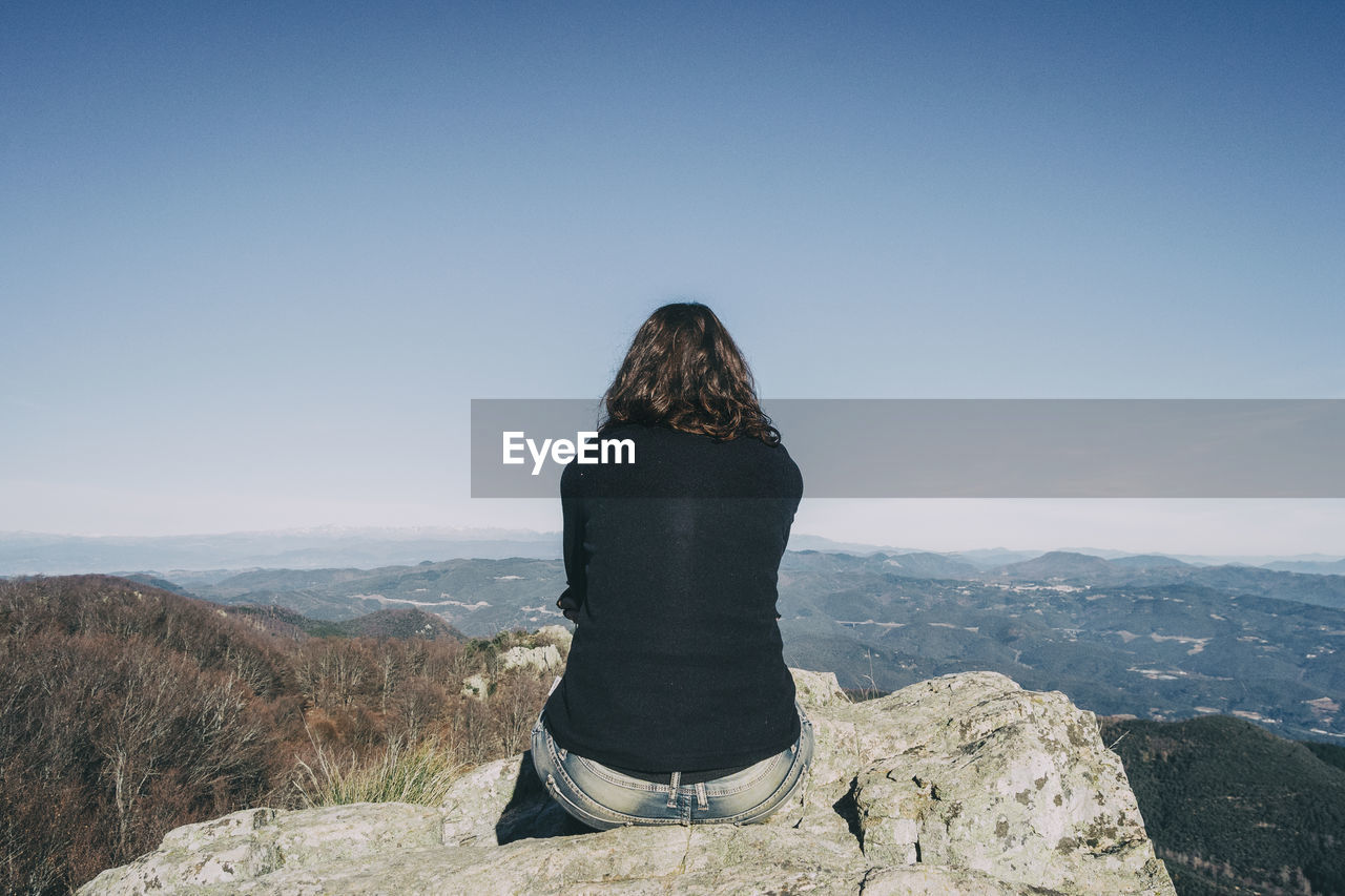 Girl from the back sitting on a top stone looking at the distant mountains