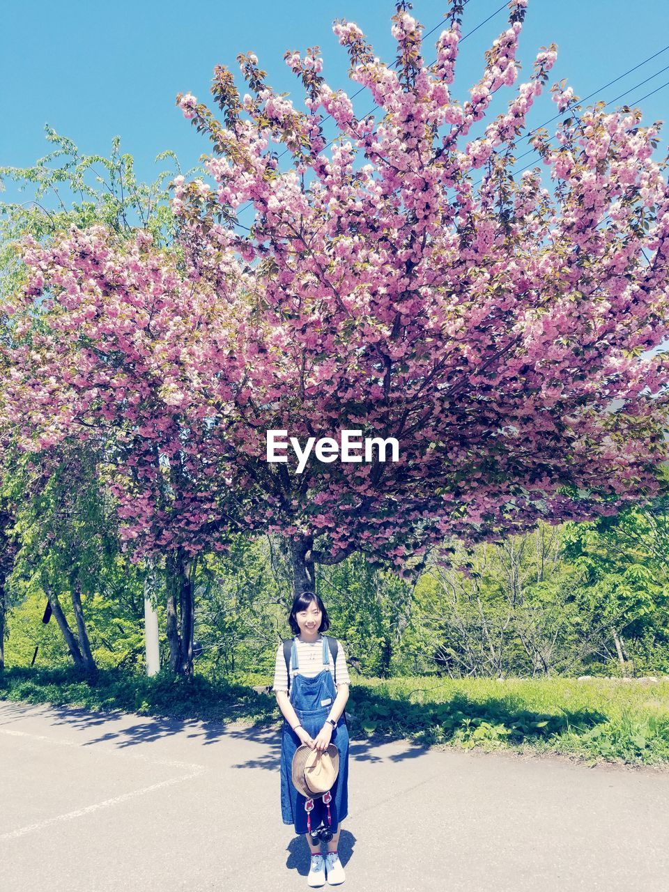 Portrait of smiling woman standing on footpath against tree at park 