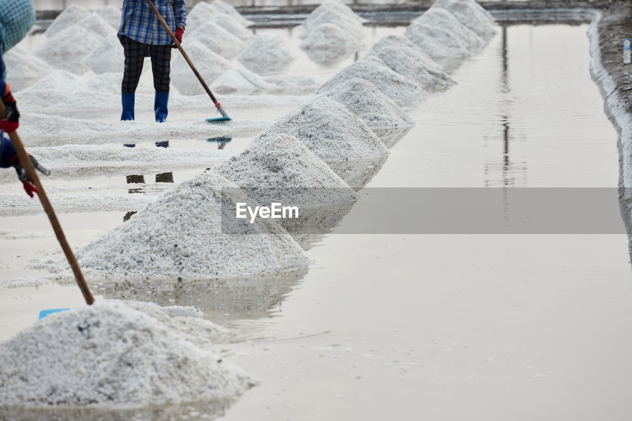 Worker using wooden rake for harvesting dried salt at salt pan