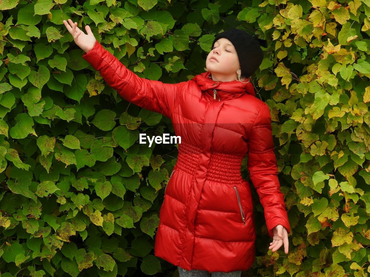 Girl in red jacket standing against plants