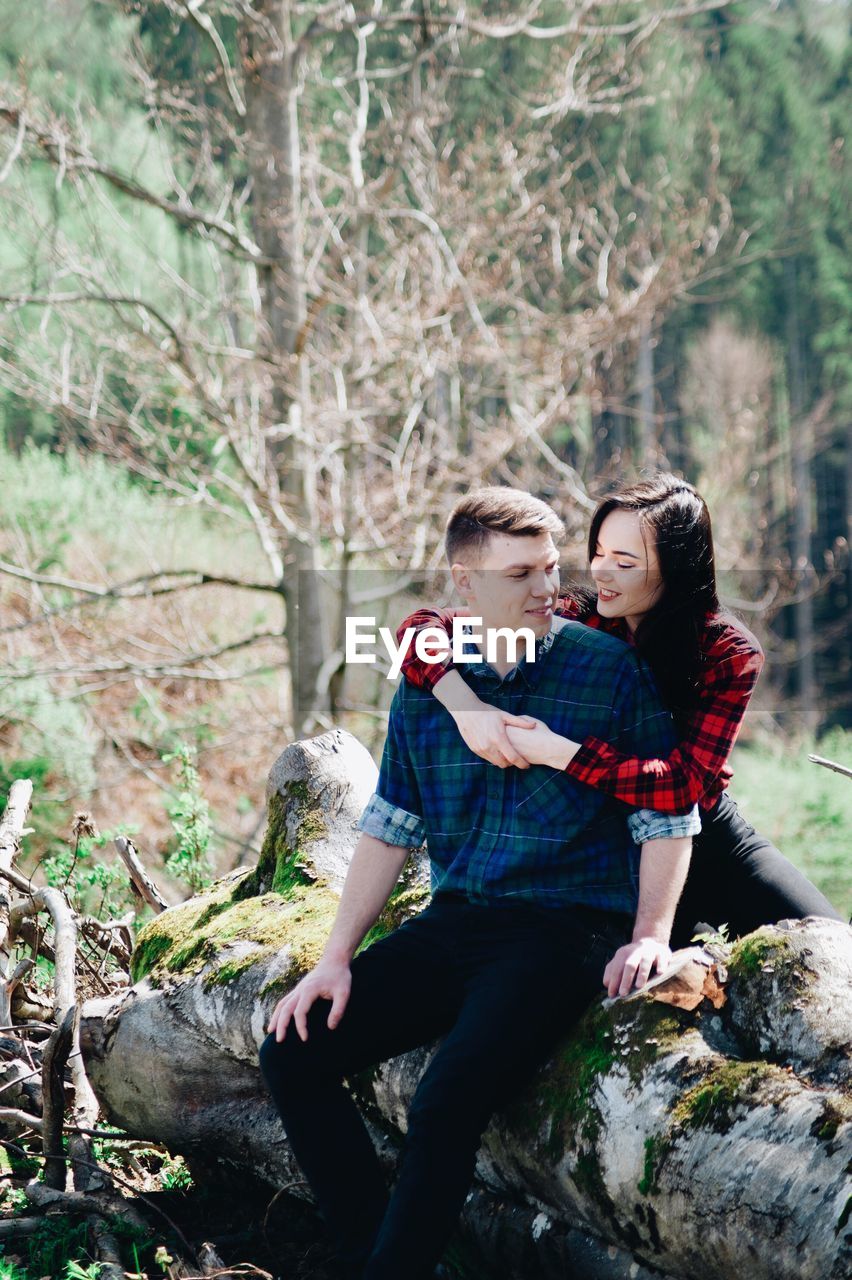Smiling girlfriend embracing boyfriend in forest