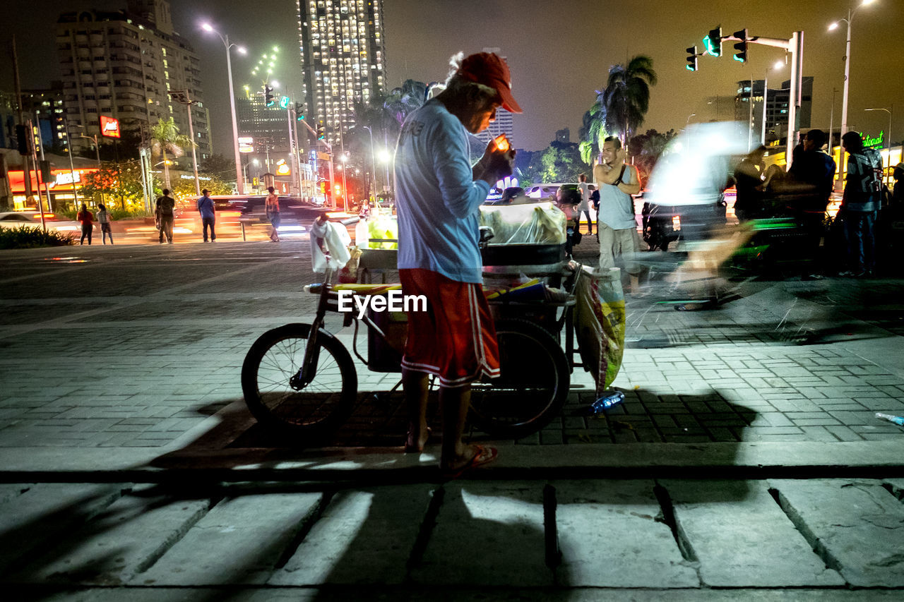 REAR VIEW OF WOMAN RIDING BICYCLE ON CITY AT NIGHT